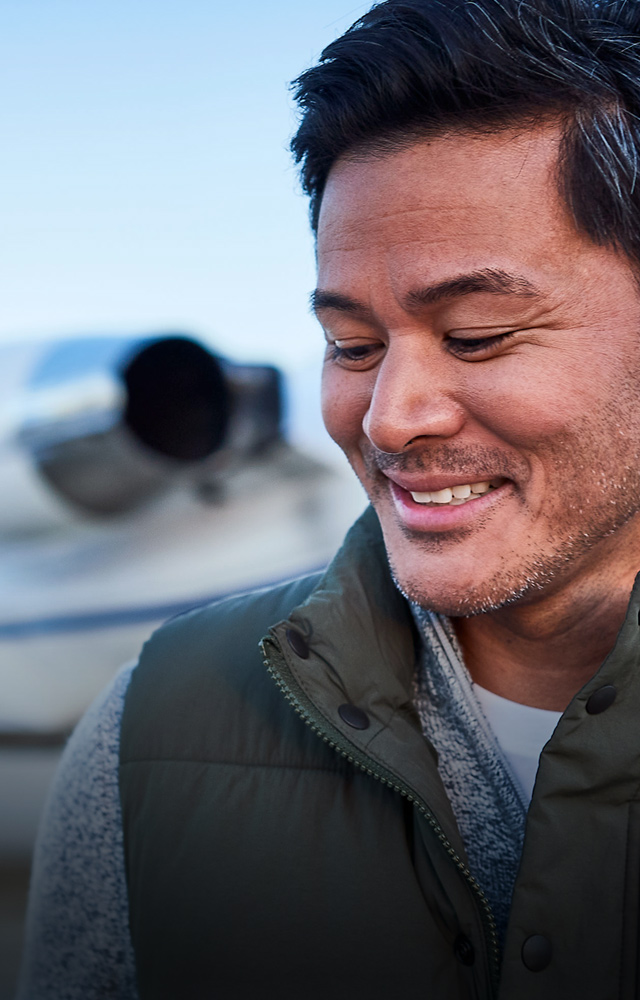 man smiling in front of private jet blurred in background