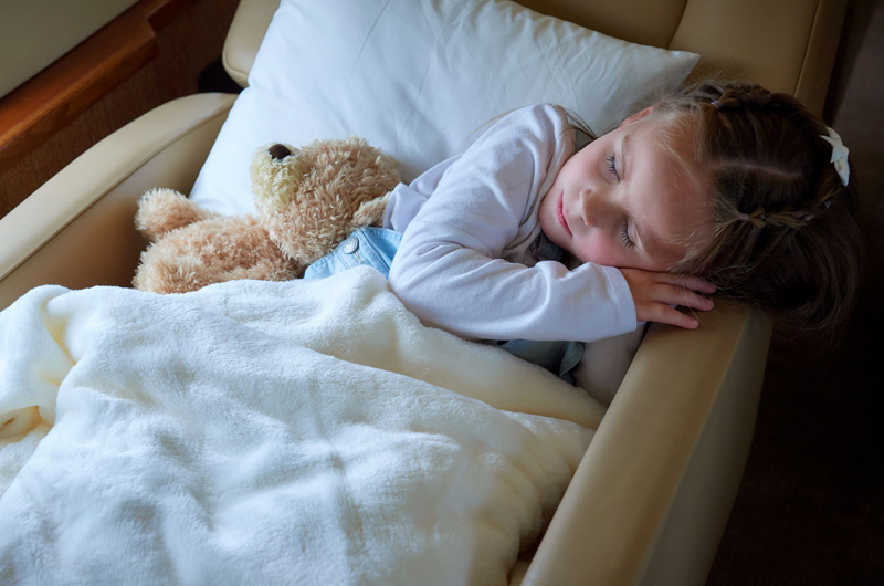 child sleeping in private jet chair with teddy bear